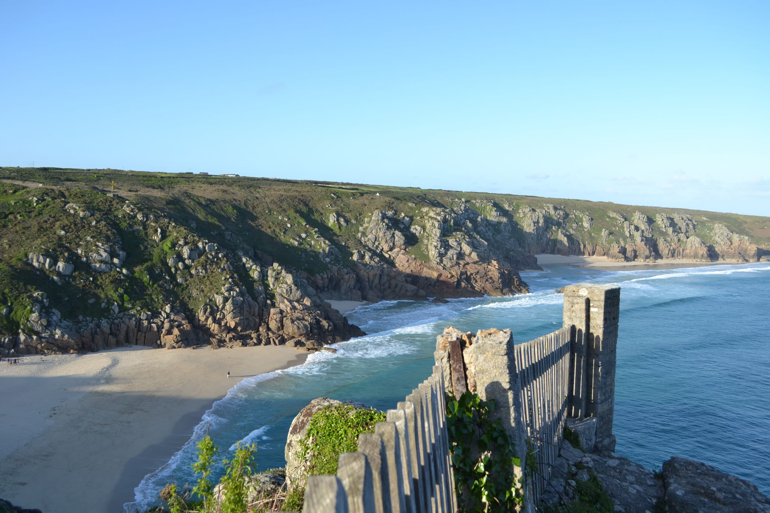 A sandy beach and granite cliffs seen from a coastal path