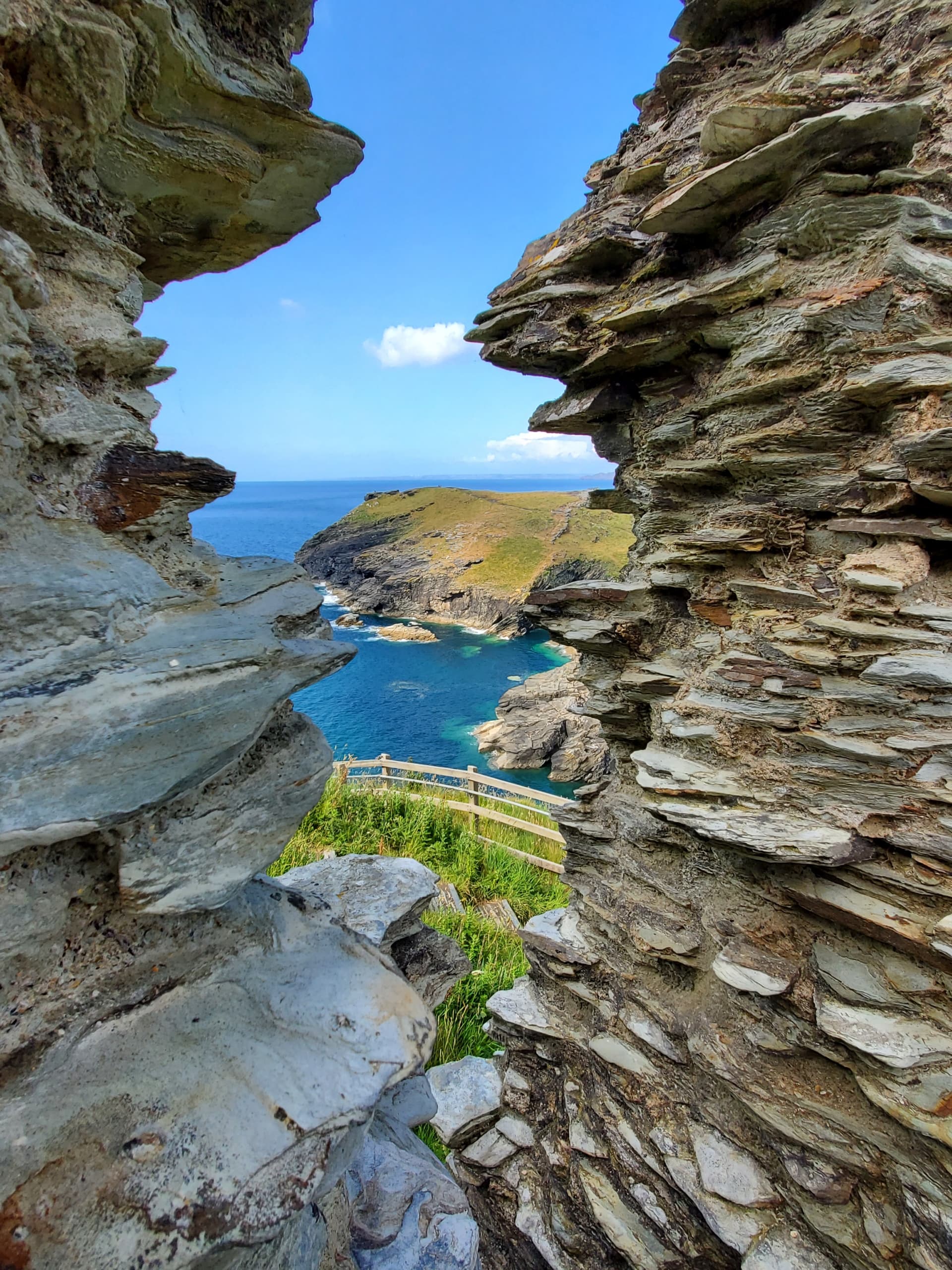 The sea and a green headland framed between jagged slate rocks at Tintagel